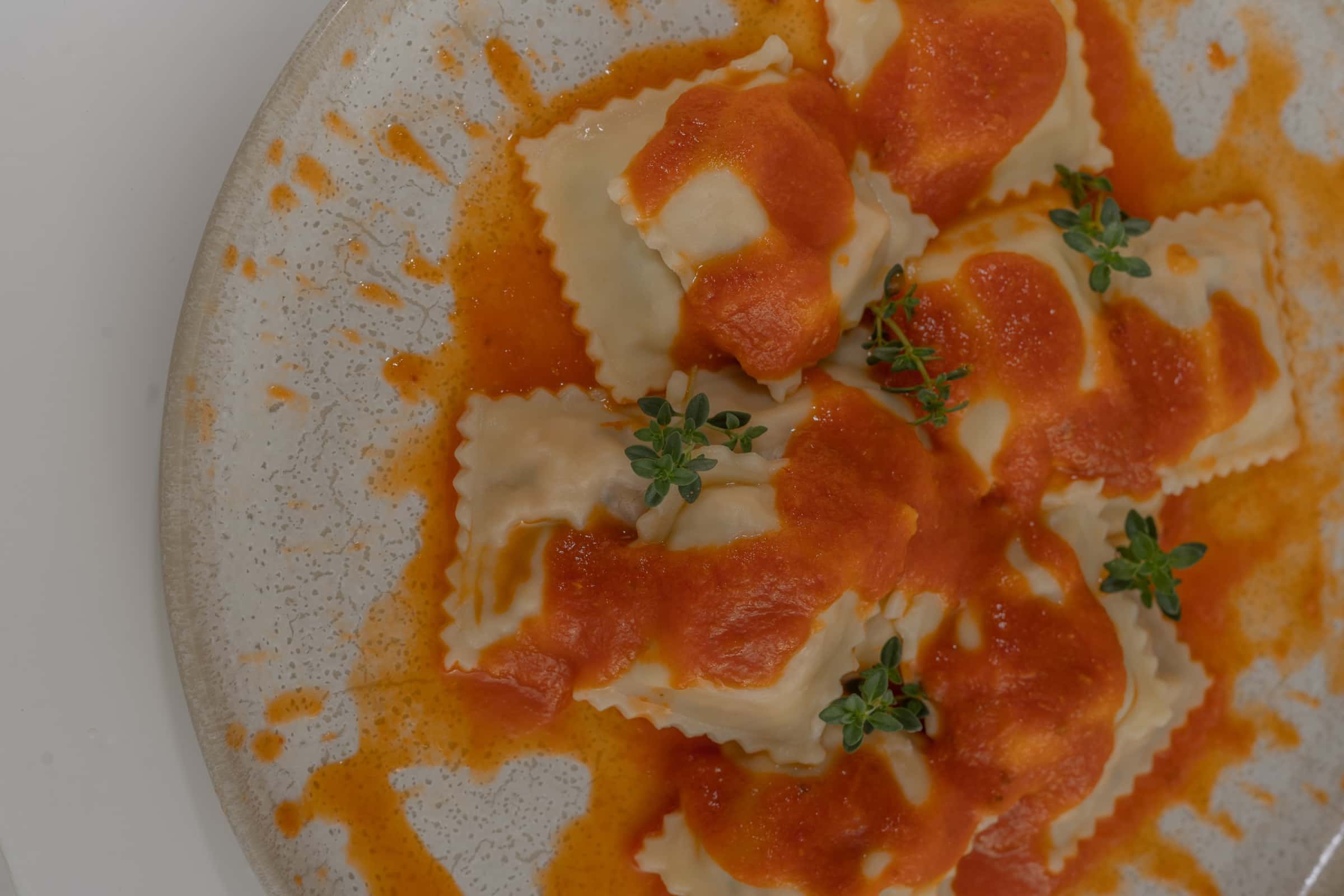 Close de ravioli ao molho alaranjado com folhas verdes, servido num prato de cerâmica rústica