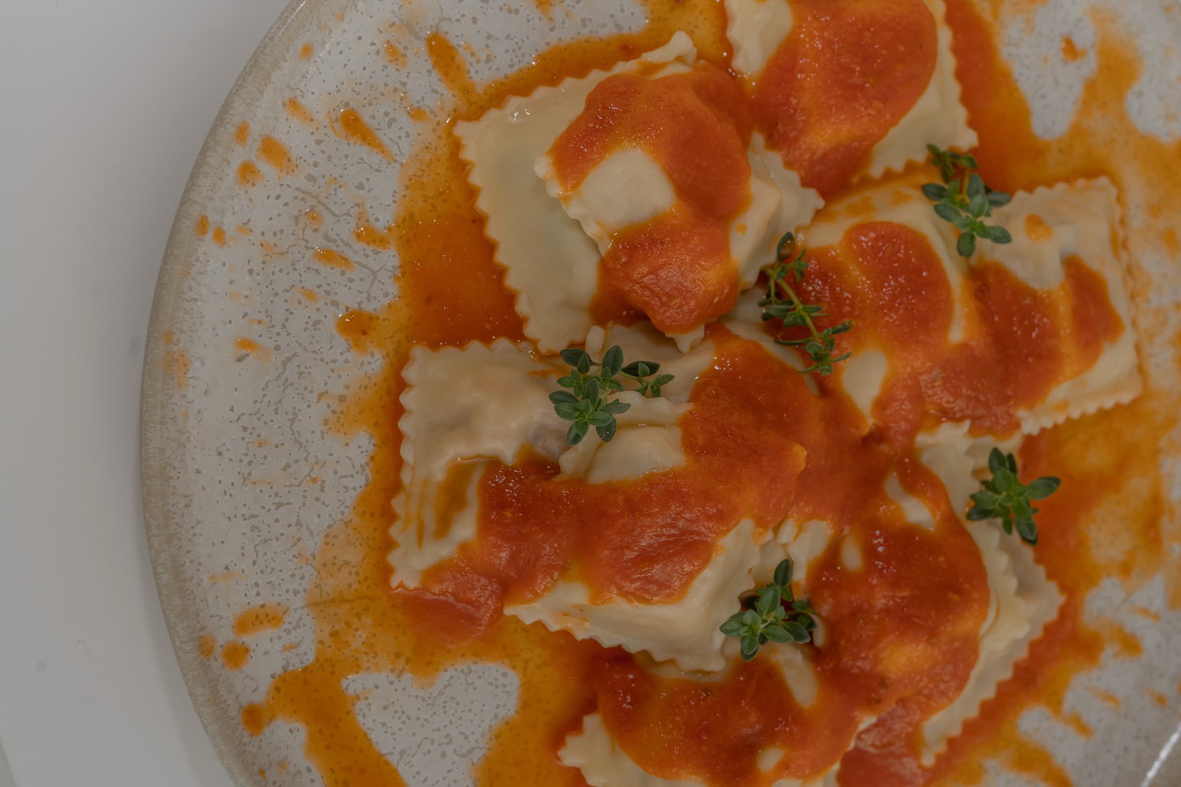 Close de ravioli ao molho alaranjado com folhas verdes, servido num prato de cerâmica rústica
