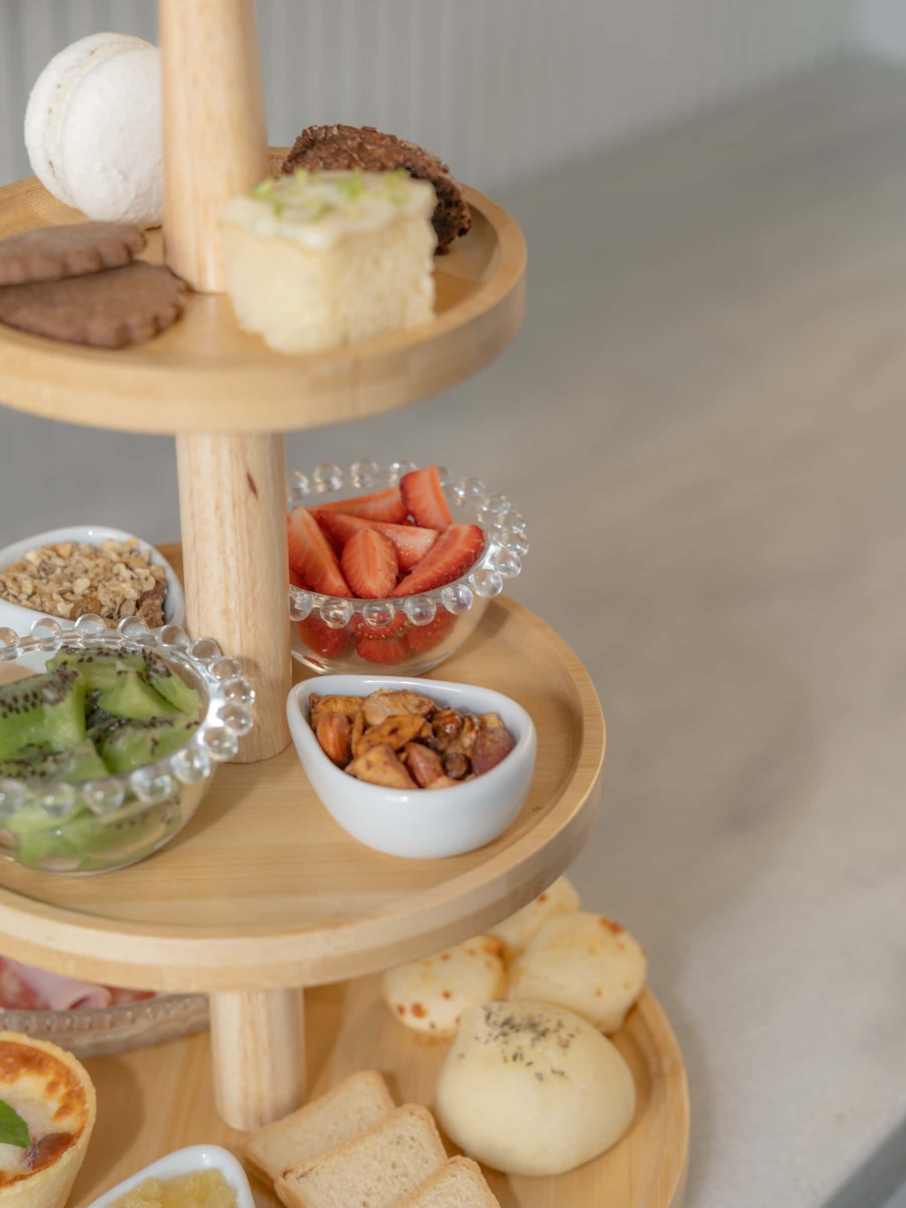 Detalhe da torre do café da manhã, com pão de queijo, macaron rosa, frutas vermelhas e pequenas porções em tigelas brancas