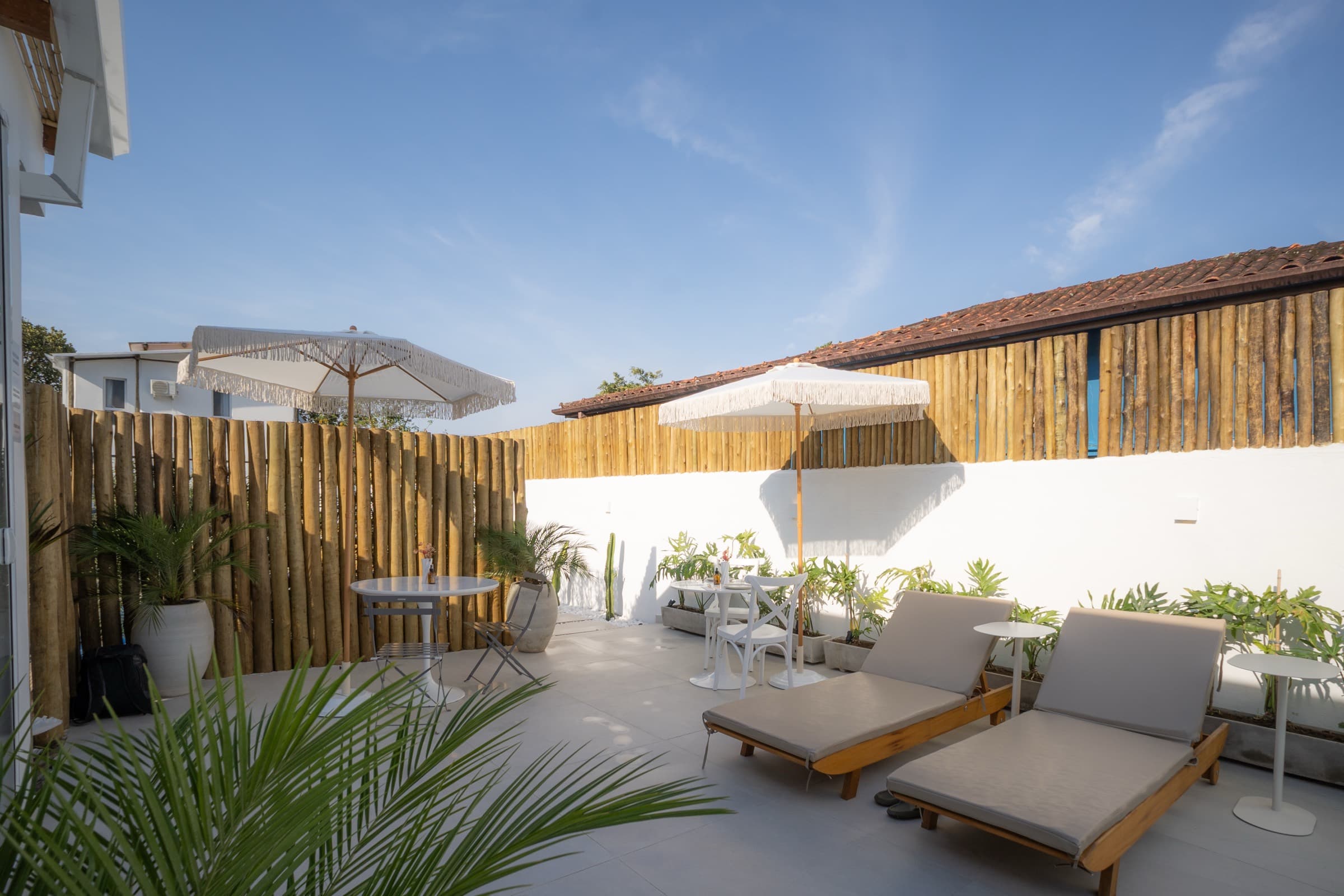 Terraço com espreguiçadeiras cinza, mesa alta e cerca de bambu, aberto para o céu